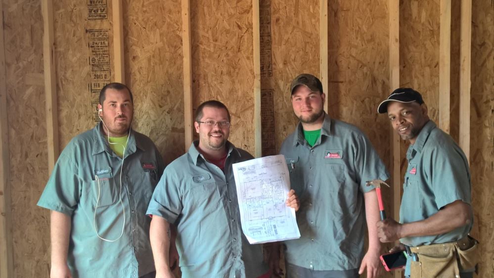 All Weather Heating & Air Conditioning team standing with a new build plan